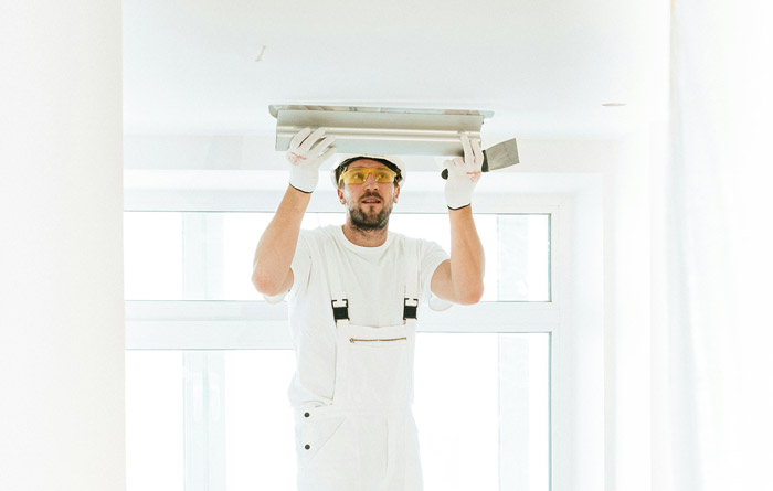 man in white overalls applying finishing layer to ceiling in bright room